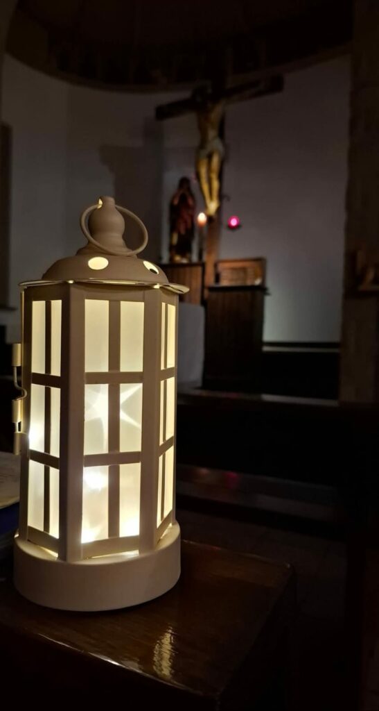 Wnętrze kościoła z krzyżem nad ołtarzem; na pierwszym planie zapalony lampion.