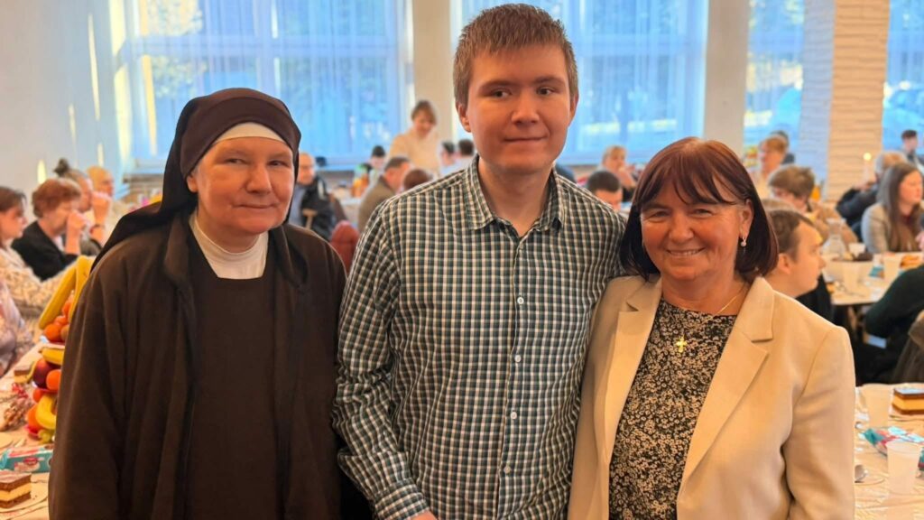 Siostra zakonna i młody mężczyzna oraz kobieta pozują uśmiechnięci do zdjęcia w tle zastawione stoły i pozostali uczestnicy spotkania.