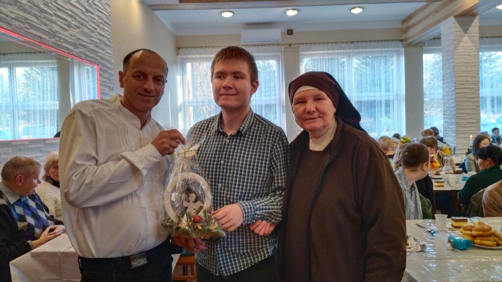 Dwóch mężczyzn i Siostra zakonna. Mężczyźni trzymają świąteczny stroik.