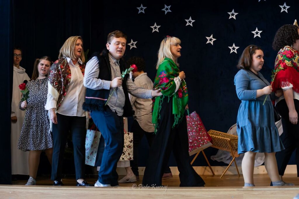 Kolejna scena przedstawienia - grupa dorosłych i dzieci idą w parach. Dzieci trzymają w rękach róże, a kobiety ubrane są w kolorowe chusty na ramionach i niosą prezenty.