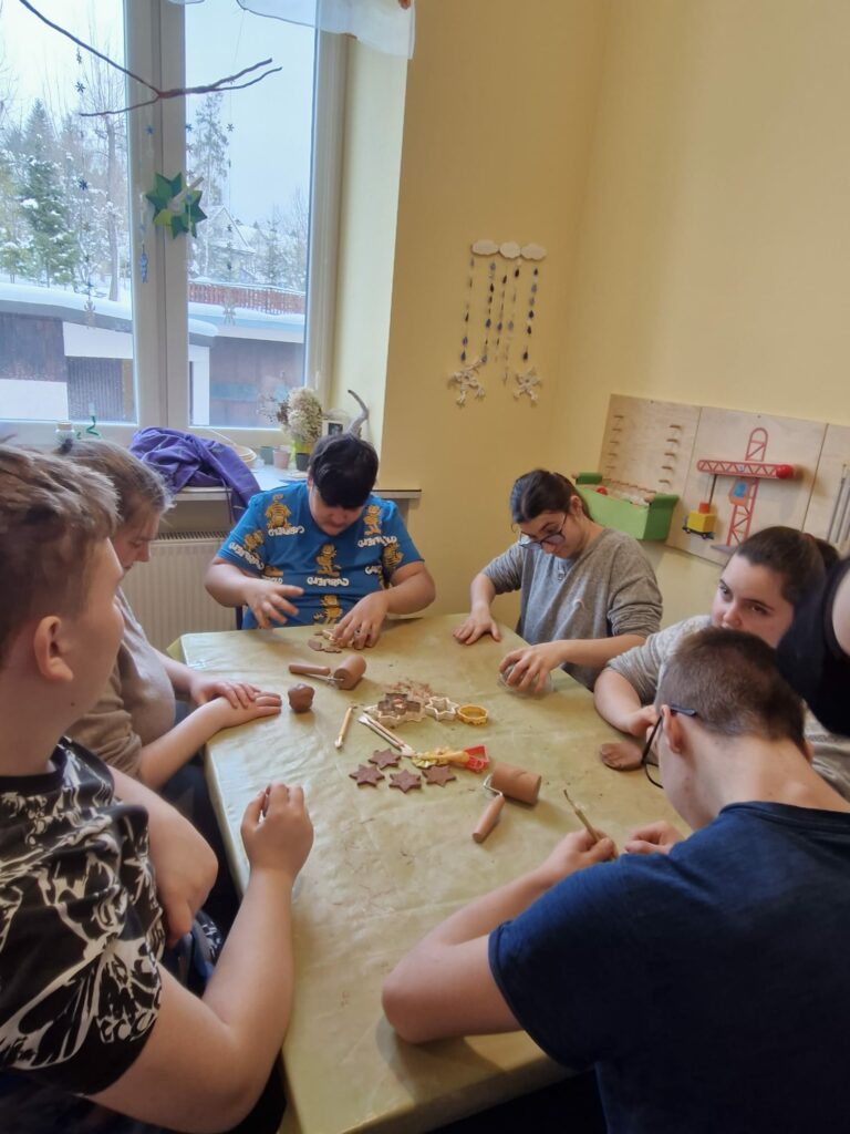 Grupa dzieci siedzi przy stole i wycina kształty z gliny.