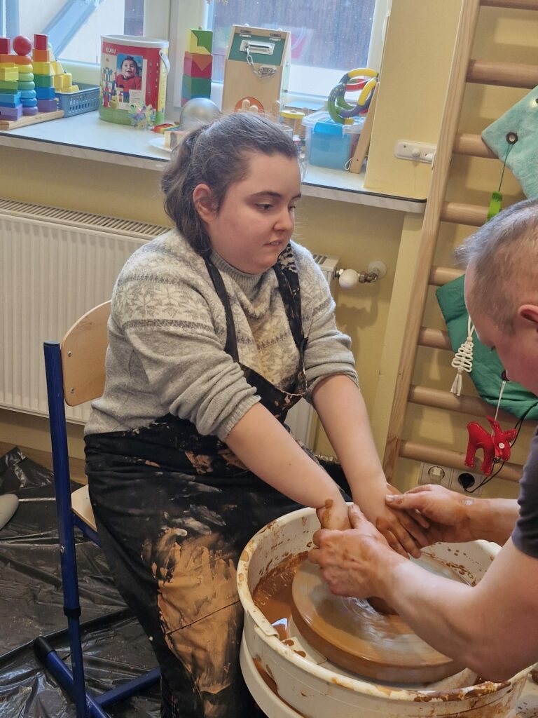 Dziewczynka formuje glinę na kole garncarskim z pomocą dorosłego instruktora.