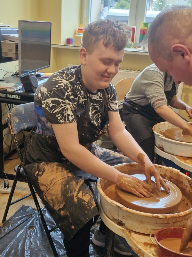 Chłopiec formuje glinę na kole garncarskim pod okiem instruktora.