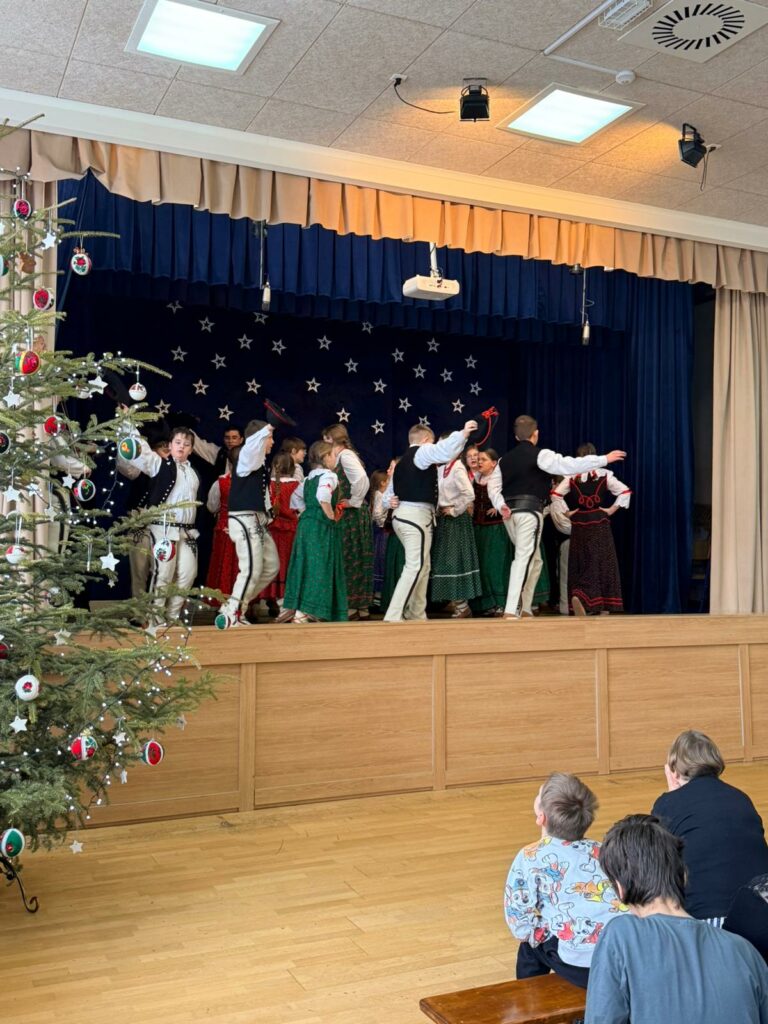 Grupa dzieci tańczy na scenie podczas szkolnego występu świątecznego.