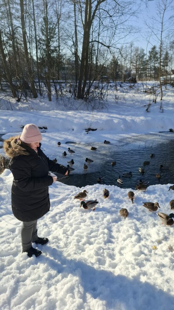 Młoda kobieta karmiąca kaczki w zimowej scenerii nad rzeką.