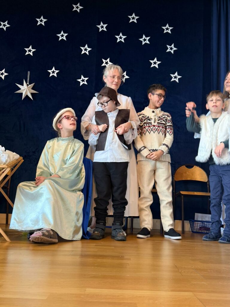 Grupa dzieci w przebraniach stoi na scenie za nimi niebo usłane gwiazdami.