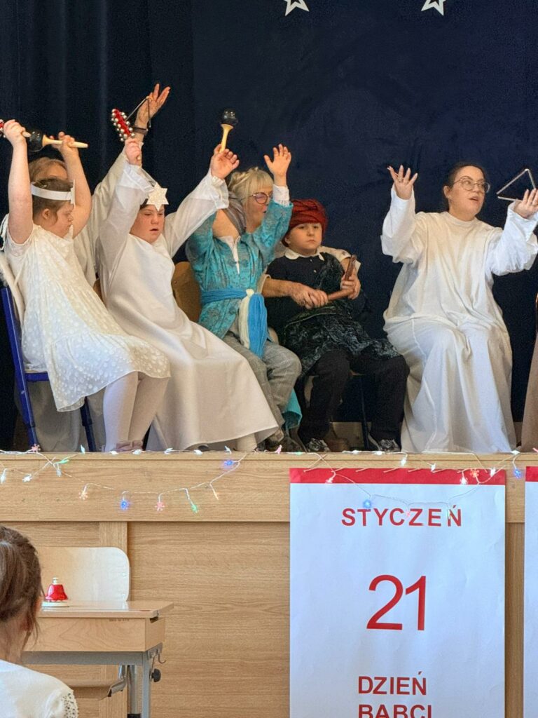 Dzieci przebrane za aniołki i królowie wznoszą ręce do góry trzymając w nich instrumenty.