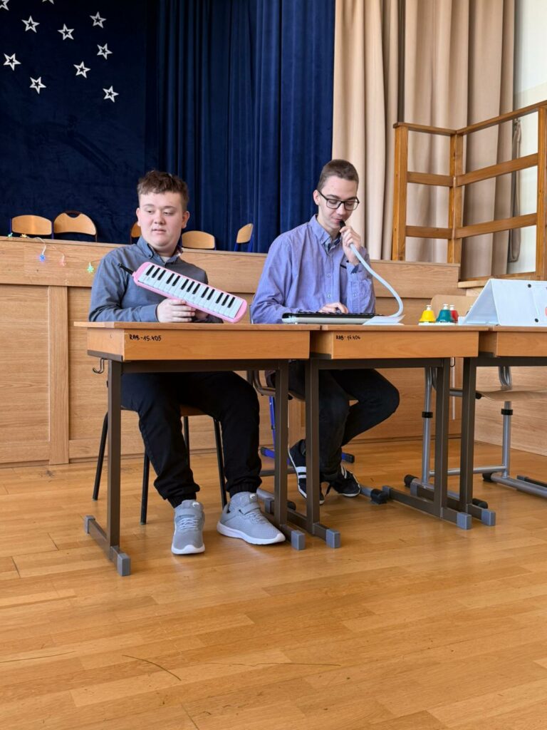 Dwóch młodych chłopców siedzi przy stolikach i grają na melodykach.