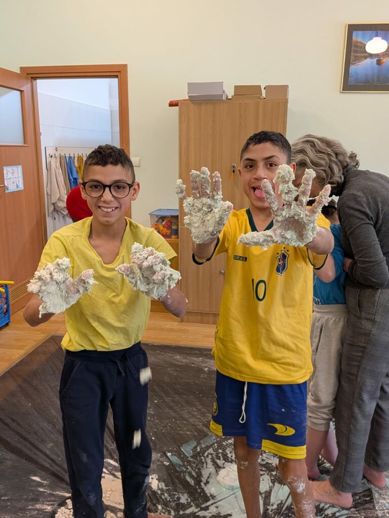 Dwóch uśmiechniętych chłopców pokazuje do aparatu dłonie całkowicie oblepione gęstą masą sensoryczną.