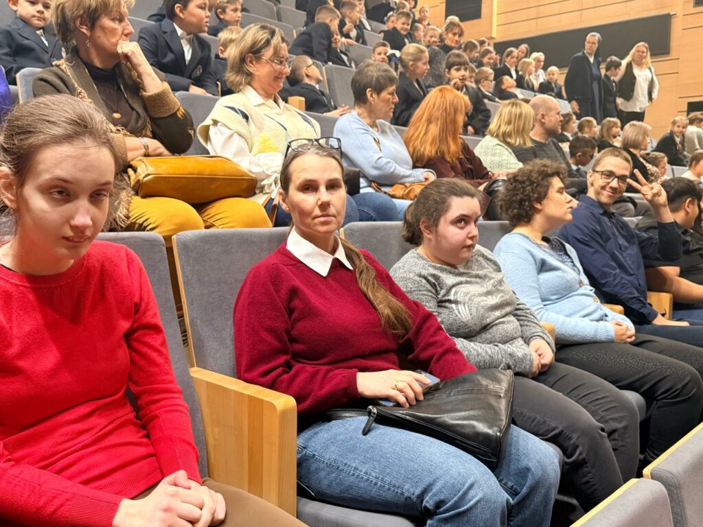 Duża grupa dorosłych i dzieci siedzi na sali teatralnej czekając na przedstawienie.