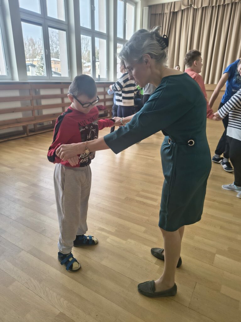 Nauczycielka pomaga chłopcu w okularach nauczyć się kroków tanecznych podczas wspólnej zabawy.