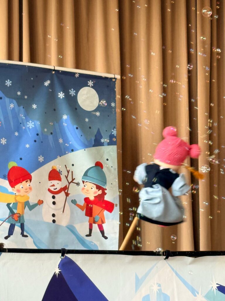 Kukiełka porusza się na scenie podczas przedstawienia, wokół unoszą się bańki mydlane.