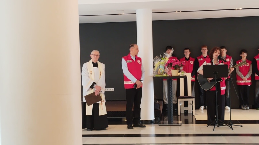 Występ muzyczny na scenie z udziałem wolontariuszy w czerwonych kamizelkach i osoby duchownej.