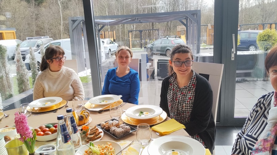 Trzy kobiety przy wspólnym posiłku przy zastawionym stole w jasnym wnętrzu.