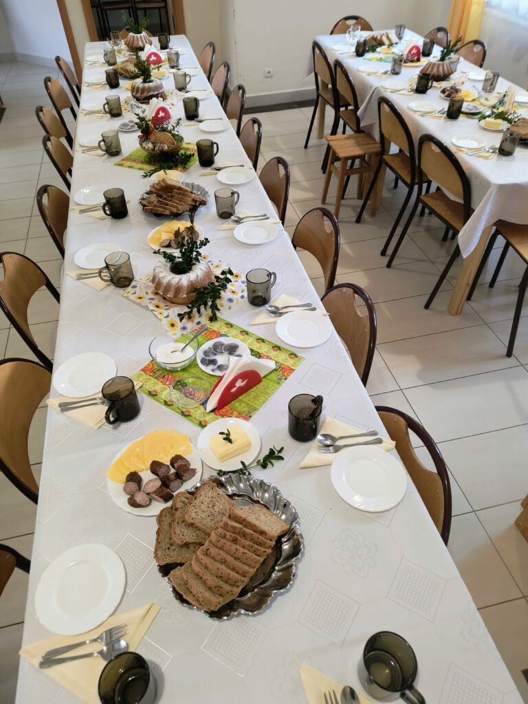 Długi stół nakryty do posiłku z pieczywem, wędlinami i wielkanocnymi dekoracjami.