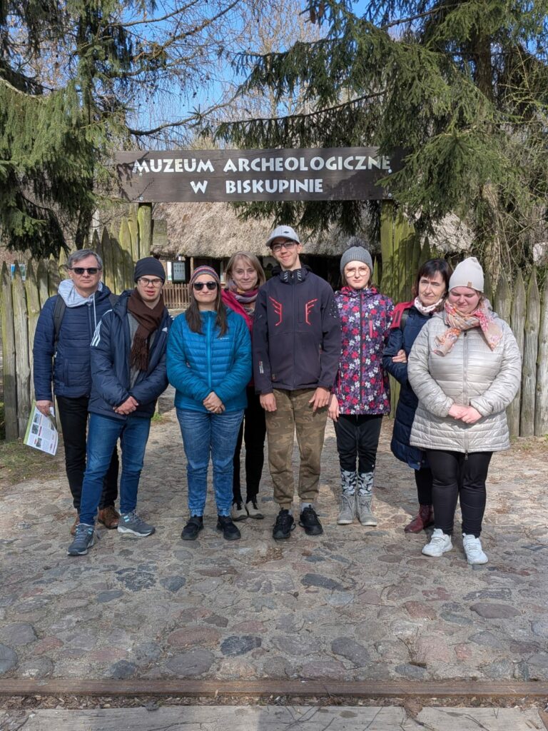 Grupa osób stoi przed wejściem do muzeum archeologicznego w Biskupinie.