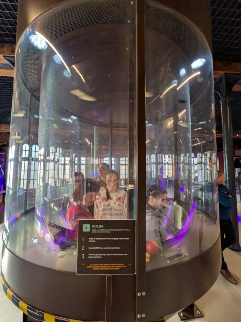 Eksponat w formie dużej szklanej tuby z osobami widocznymi w środku.