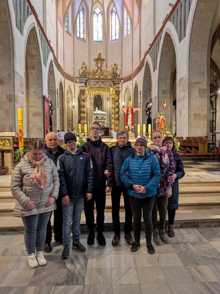 Grupa osób stoi wewnątrz zabytkowej katedry o wysokich sklepieniach, pozując przed ołtarzem w kościele.