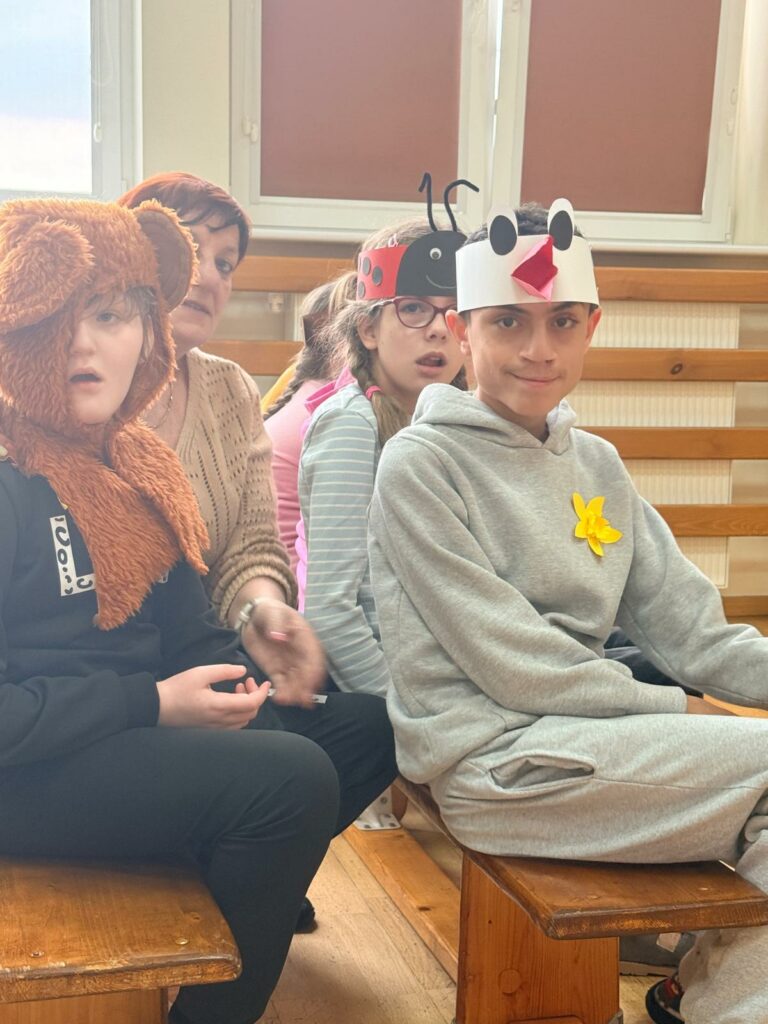 Dzieci siedzą obok siebie w sali, mają na głowach opaski z motywami zwierząt, patrzą w stronę aparatu.