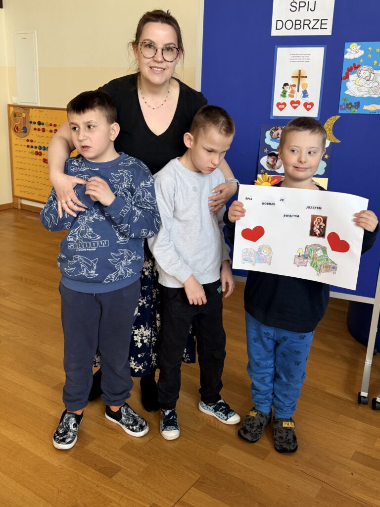 Kobieta i trzech chłopców, jeden z nich trzyma pracę z obrazkiem świętego.