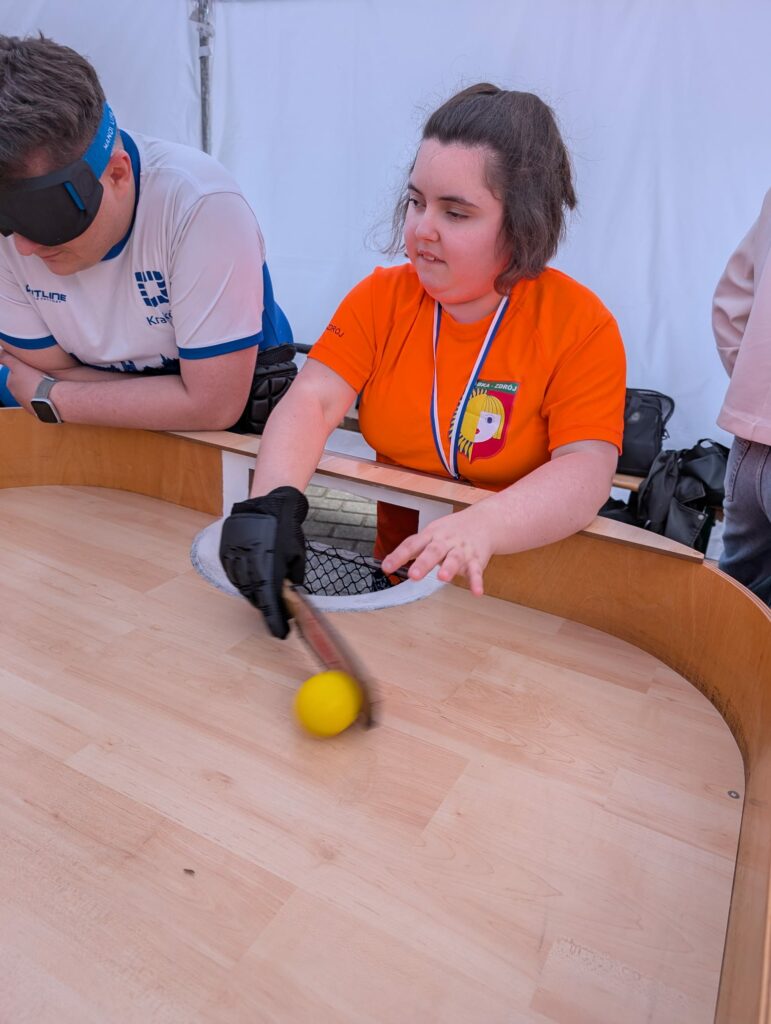Młoda kobieta gra w showdown, obok stoi mężczyzna w opasce zasłaniającej oczy.
