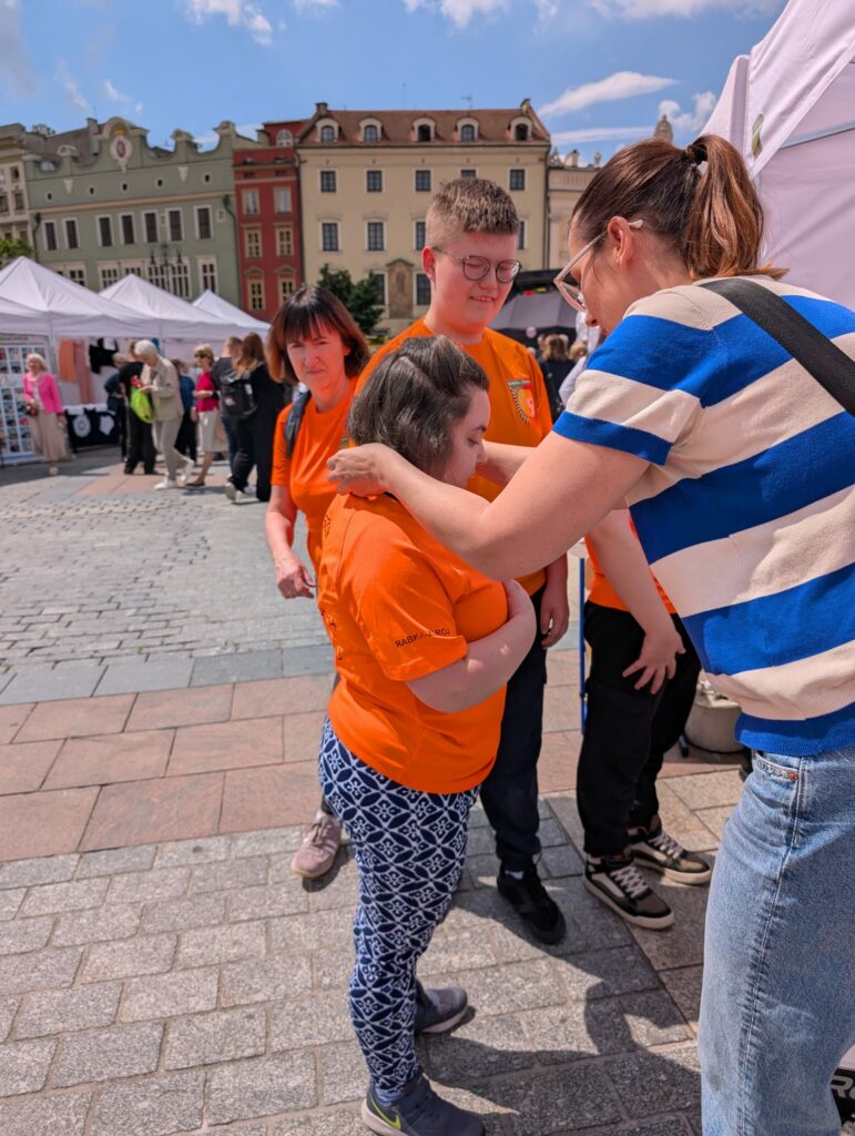 Kobieta wręcza medal uczestniczce w pomarańczowej koszulce, obok stoją inni uczestnicy wydarzenia.