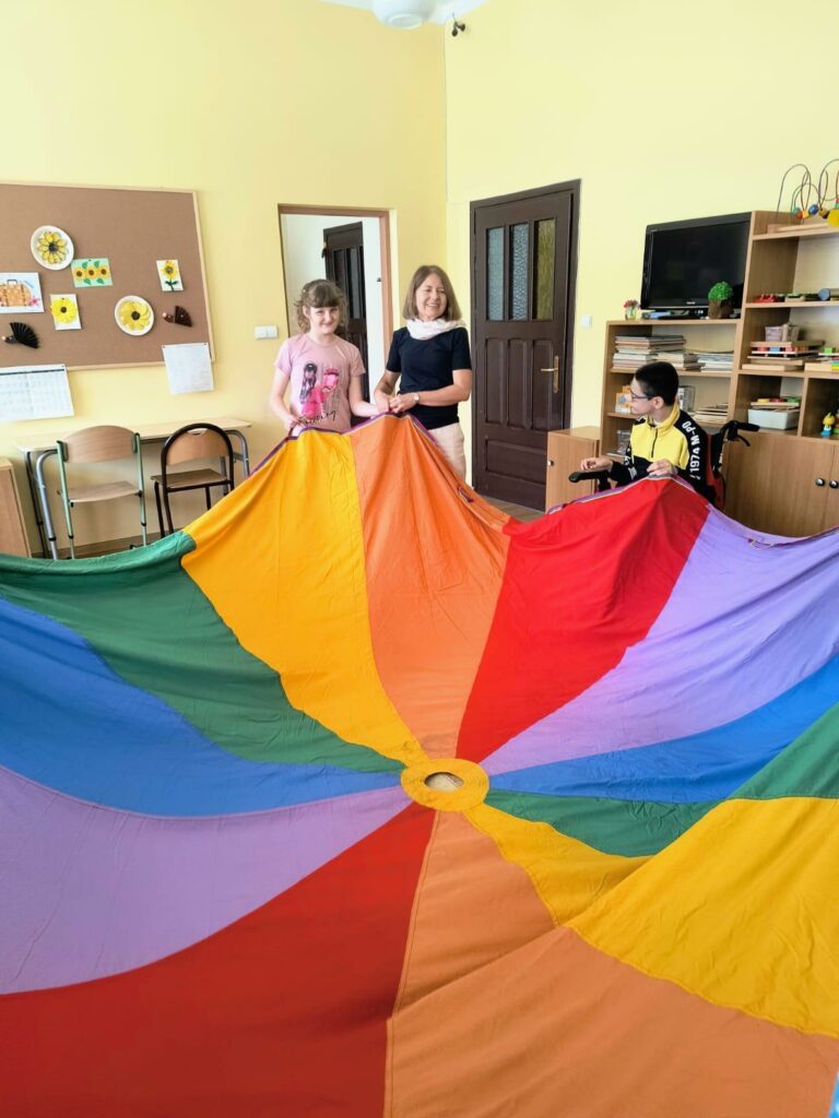 Dzieci i nauczyciele bawią się dużą, kolorową chustą animacyjną.
