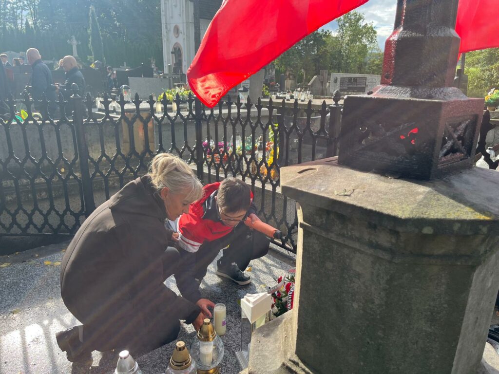 Kobieta i chłopak klęczą przy pomniku na cmentarzu i zapalają znicz.