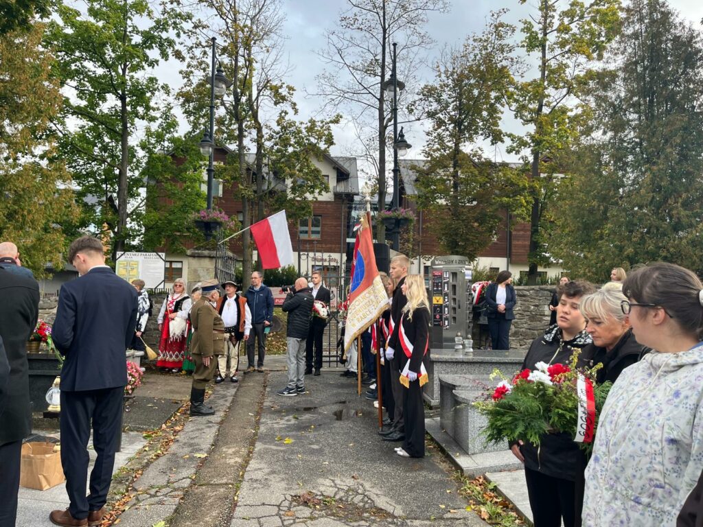 Uczniowie i pracownicy szkoły uczestniczą w uroczystości patriotycznej przy pomniku, składając kwiaty i wieńce.