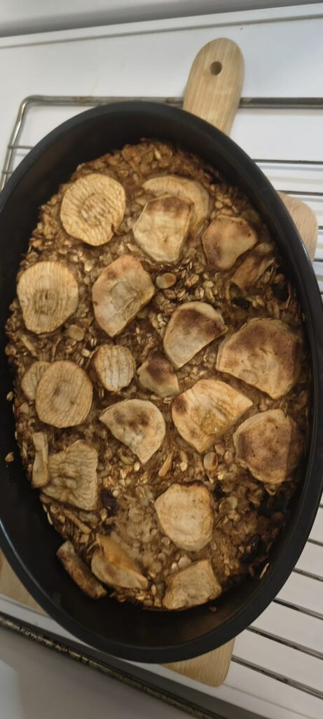 Czarna forma do pieczenia wypełniona zapieczoną owsianką z plastrami jabłka na wierzchu.