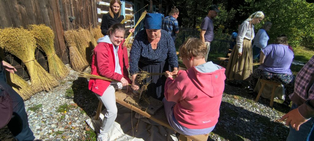 Uczniowie poznają tradycyjną metodę obróbki lnu, pracując wspólnie przy drewnianym narzędziu.