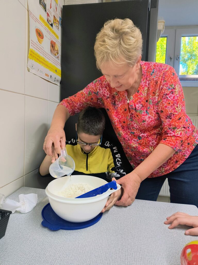 Uczeń z pomocą nauczycielki wsypuje składniki do miski i przygotowuje ciasto.