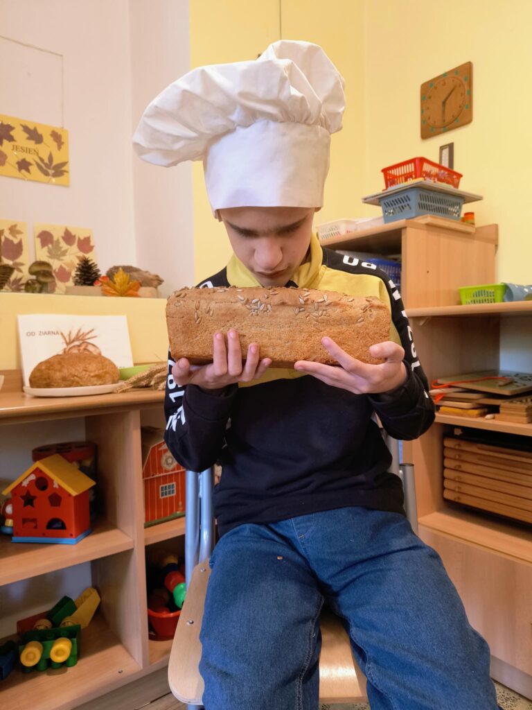 Uczeń w czapce kucharskiej trzyma upieczony chleb i poznaje efekt wspólnej pracy.