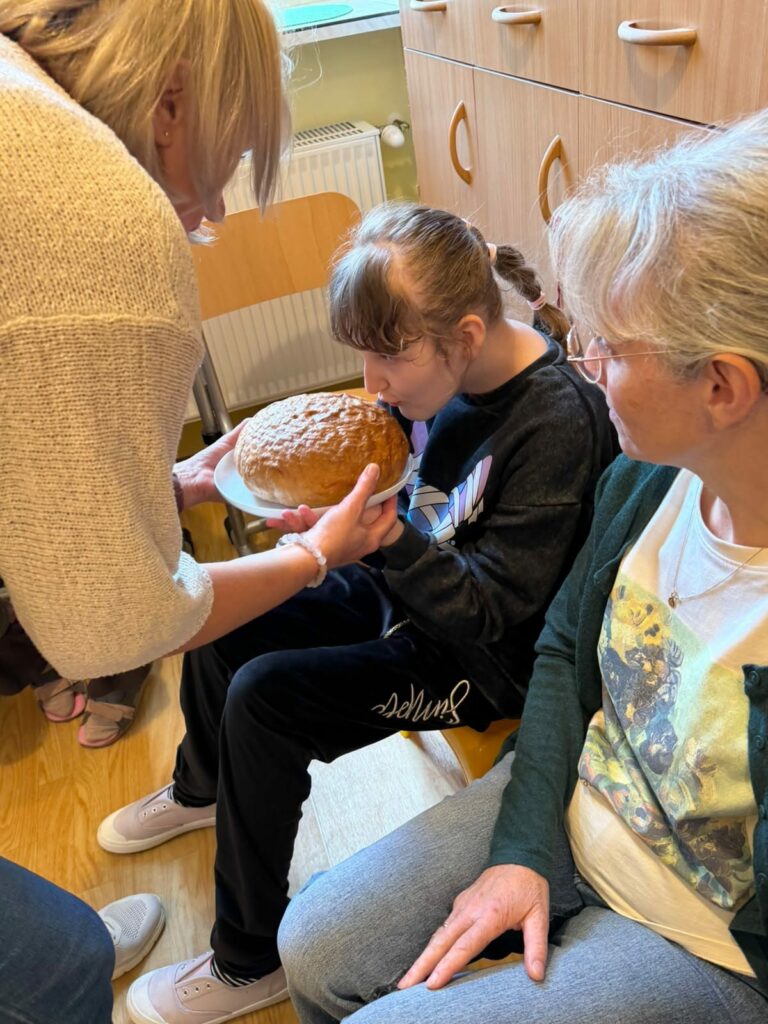 Uczennica poznaje zapach świeżo upieczonego chleba z pomocą nauczycielek.
