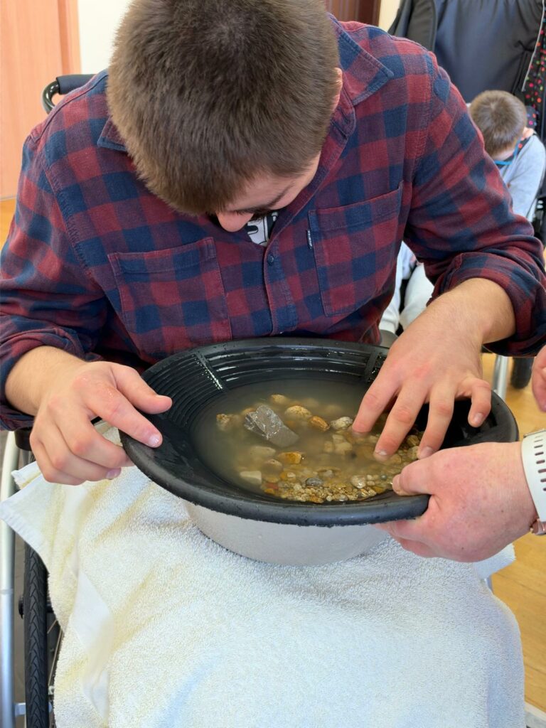 Uczeń dotyka kamieni zanurzonych w wodzie, poznając ich fakturę.