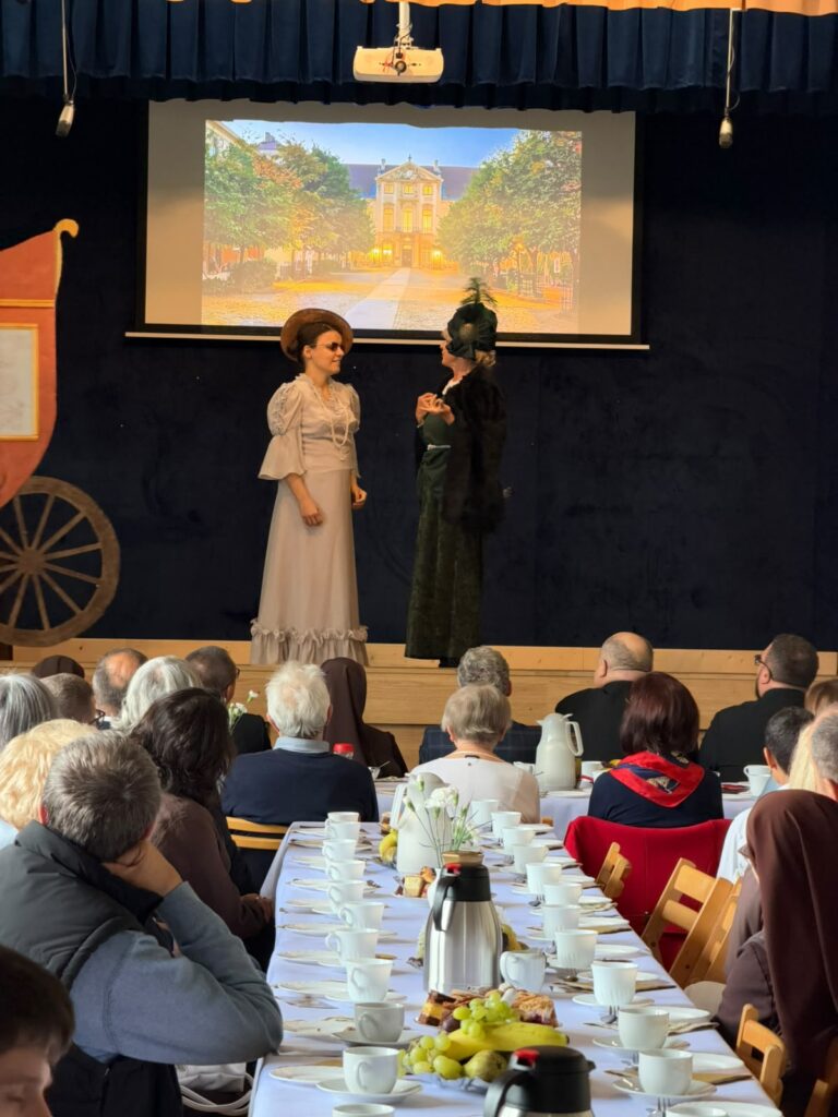 Dwie kobiety w strojach z epoki prowadzą rozmowę na scenie podczas przedstawienia.