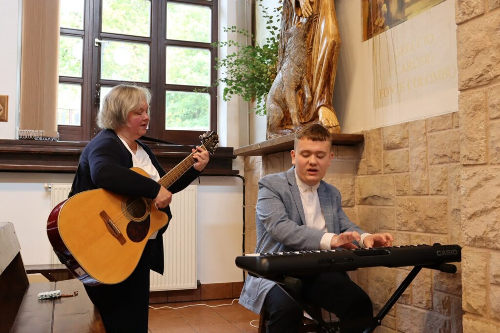 Kobieta gra na gitarze, a uczeń w garniturze gra na keyboardzie podczas uroczystości.